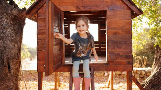 Smiling child in a wooden treehouse-style playhouse.