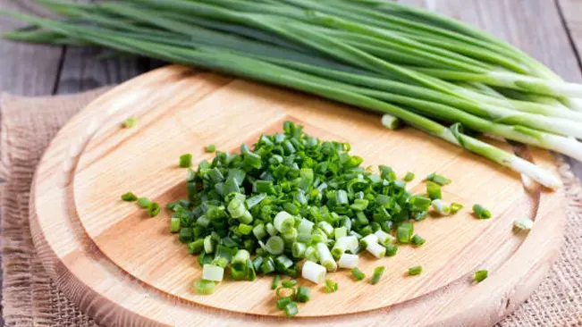 Chopped chives on a wooden cutting board with whole chives alongside, illustrating their common use in cooking.