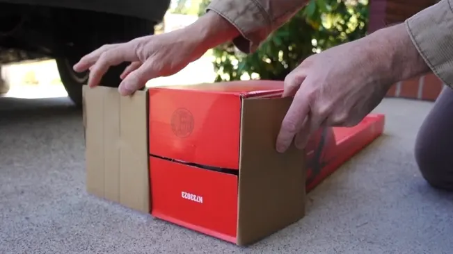 Person unboxing a hedge trimmer from a red and brown box