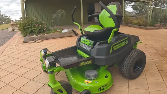 green and black ride-on lawnmower, model CRZ 426, parked on a brick pavement in front of a house.