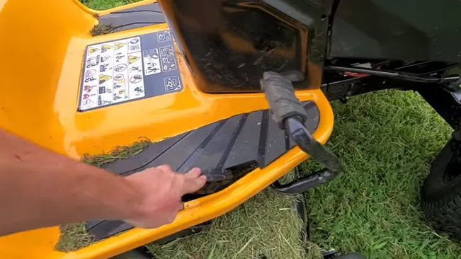 person’s hand reaching towards the underside of a modern yellow lawnmower, possibly for inspection