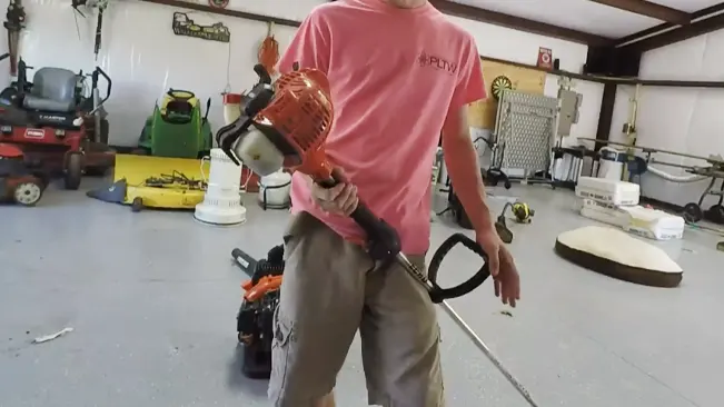 Person in a garage, holding a chainsaw with various tools in the background