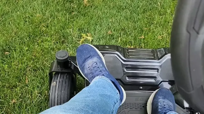 Person’s feet in blue sneakers on a black footboard, green grass in the background