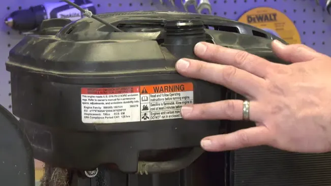 Hand holding a black mechanical part with warning labels