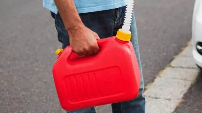 Person holding red gas canister near car