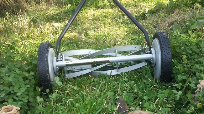 manual lawnmower with two large wheels and metallic cutting blades, placed on a grassy area that appears to be in the process of being mowed