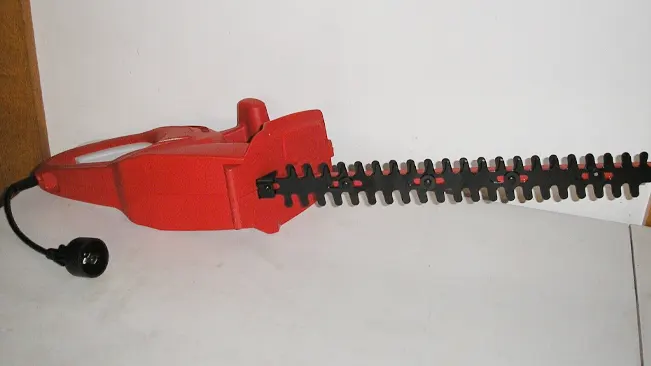 Red electric hedge trimmer on a white background.