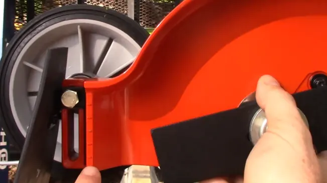 person assembling a bright red wheel edger in an outdoor setting, indicating some sort of construction or gardening activity.
