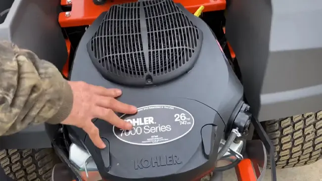 person’s hand touching the top of a KOHLER 7000 Series 26 HP engine mounted on an orange vehicle