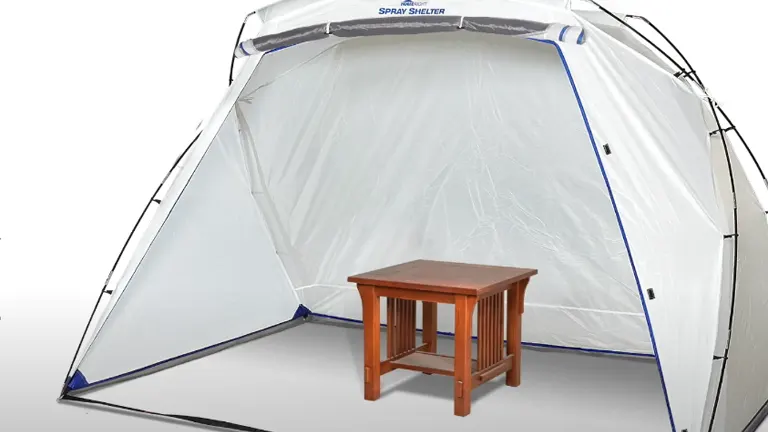 A HomeRight Spray Shelter with blue trim, set up and ready for use, with a small wooden table placed inside for painting projects.