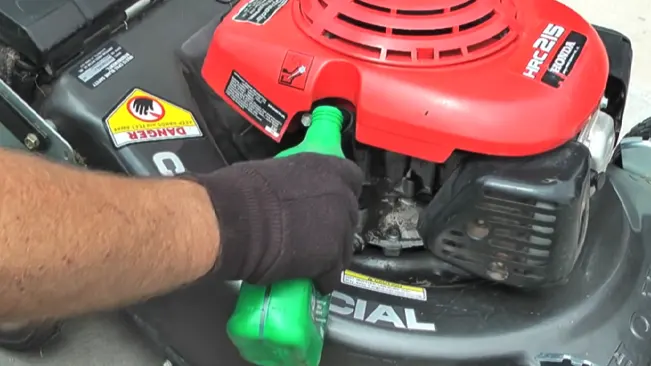 Person refilling a lawnmower’s oil with a green container.