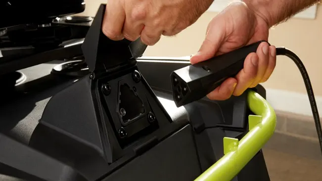 Person connecting a power plug to a black machine with a green handle in an indoor setting