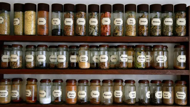A well-organized collection of spices in glass jars on a rack.
