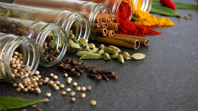 A close-up of a variety of colorful spices in glass jars on a wooden table.
