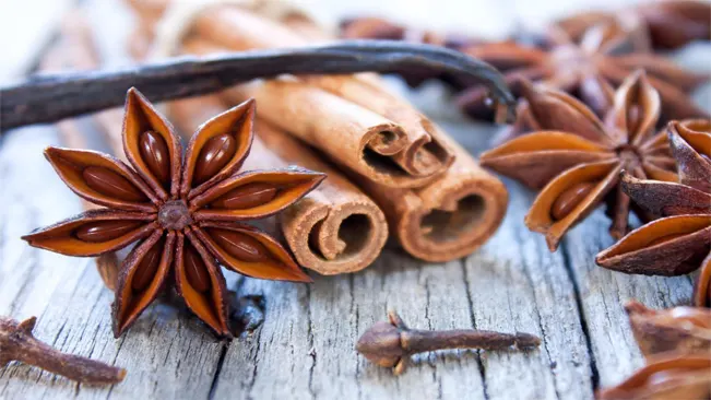 Close-up of star anise, cinnamon sticks, cloves, and a vanilla bean on a wooden table.
