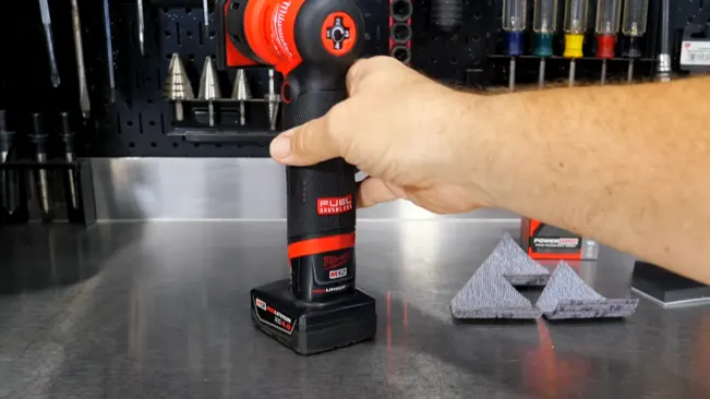 Hand holding a cordless sander at a workbench