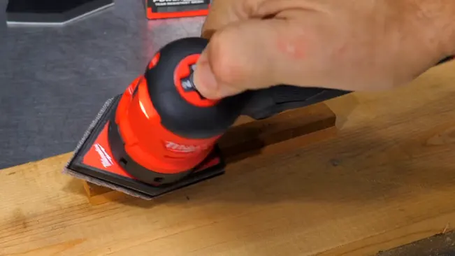 person using a red and black orbital sander on a wooden surface