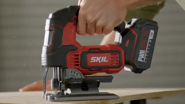 Person using a SKIL cordless jigsaw to cut a wooden board