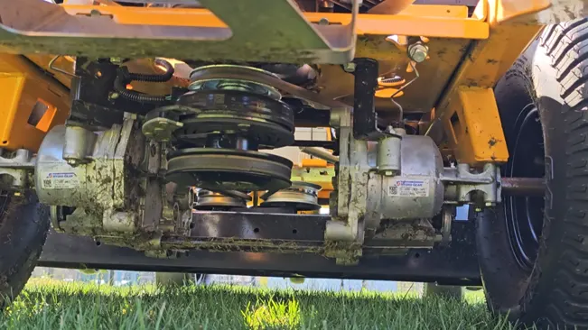 undercarriage of a yellow lawnmower showing wheels, belts, and motor on grass