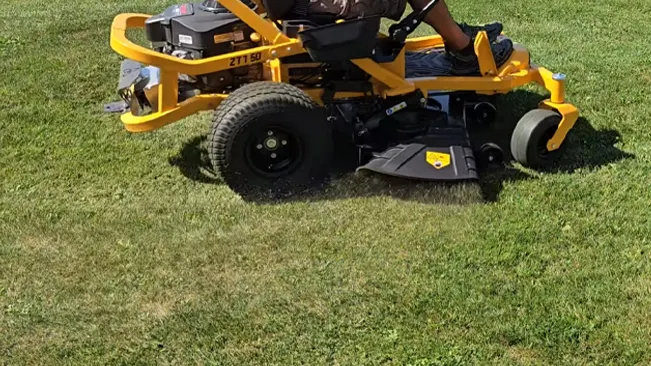 Person operating a yellow riding lawnmower on a sunny day