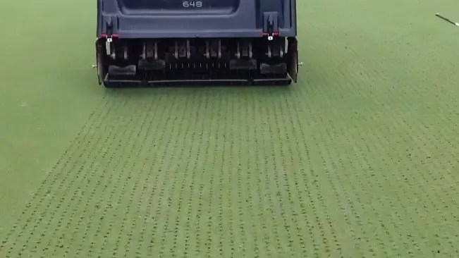 large, dark-colored machine with the number “648” actively aerating a uniformly green and flat field, leaving visible patterns of small holes across the surface.