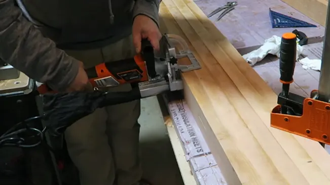 Person cutting a wooden plank with a power tool on a workbench.