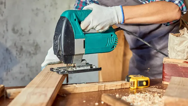 Person using a green jigsaw to cut a wooden plank