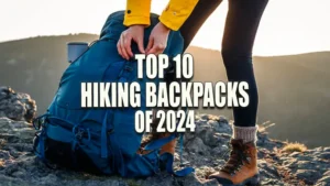A person in hiking boots and a yellow jacket securing a blue backpack on rocky terrain during sunset.
