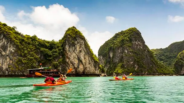 Tourists in red kayaks enjoying a sunny day amidst the towering karst limestone formations in a scenic bay.
