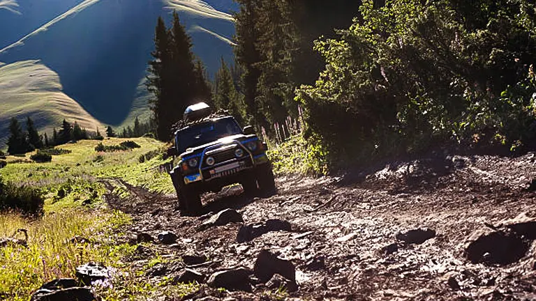 A four-wheel-drive vehicle navigating a rocky mountain trail under a bright sky.
