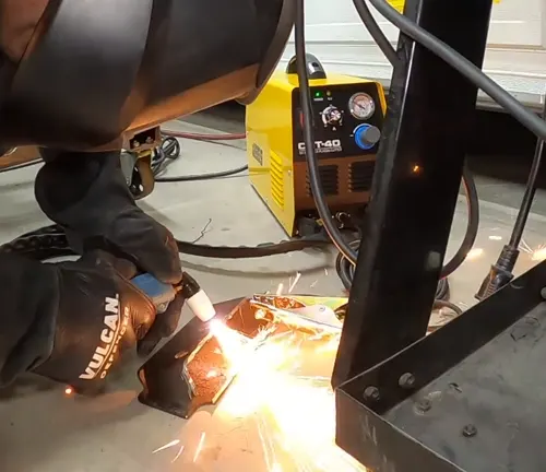 Close-up of a JEGS plasma cutter in use, with a person wearing protective gear cutting metal and sparks visible.