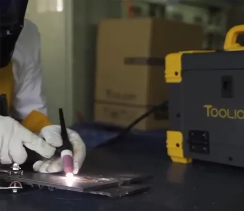 Person welding with a Tooliom welder in the background.