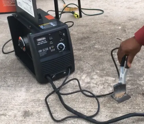 Ironton 125 Flux-Cored Welder on the ground with a hand holding the welding gun.