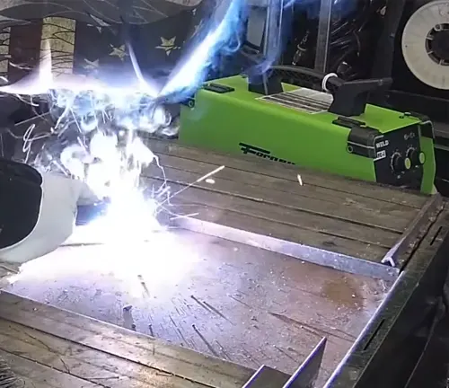 Bright arc welding sparks from Forney Easy Weld 140 FC-I, with welder's gloved hand and green machine in view.