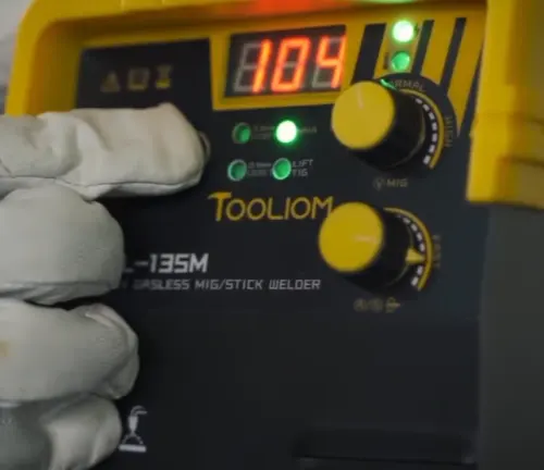 Gloved hand adjusting the settings on a Tooliom TL-135M welder display.