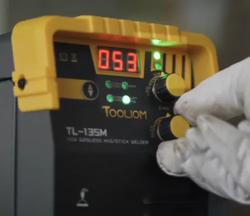 Gloved hand adjusting the dial on a Tooliom TL-135M welder.