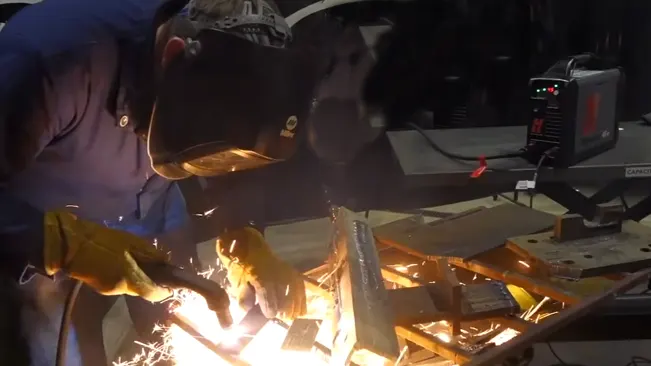 Welder in protective gear using Hypertherm Powermax45 XP to cut metal, with bright sparks flying.