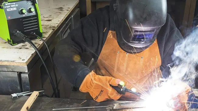 Welder in protective gear using the Forney Easy Weld 140 FC-I, with sparks flying during welding.