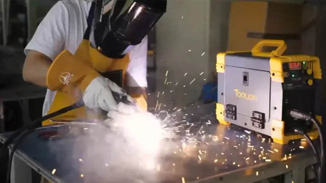 Welder in protective gear using a Tooliom welder, with sparks flying.