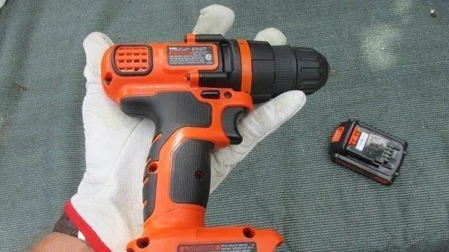 Gloved hand holding an orange and black BLACK+DECKER cordless drill with a separate battery pack.