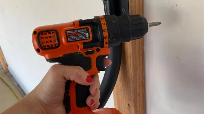 Hand holding an orange and black BLACK+DECKER cordless drill in use.