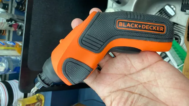 Hand holding a BLACK+DECKER 4V MAX Cordless Screwdriver (BDCS20C) with bit inserted, orange and black design