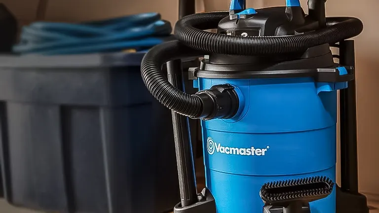 Blue Vacmaster dust collector with hose attached, set in a workshop environment