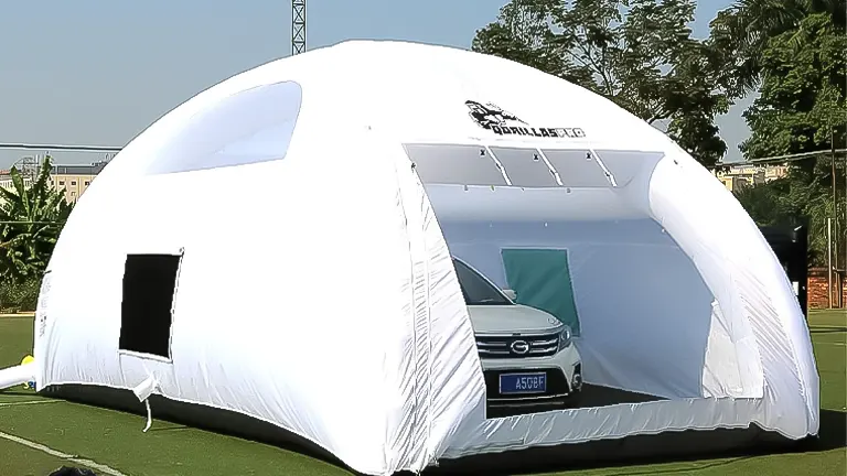 A large white dome-shaped inflatable paint booth with a car inside, positioned on a green outdoor area