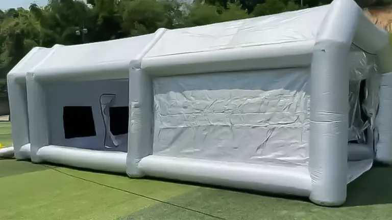 Side view of a large, white, inflatable paint booth with covered windows and entrance, set up on a grassy area