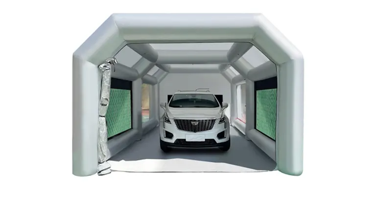 Inside a gray inflatable paint booth with a car parked centrally, flanked by green air filters