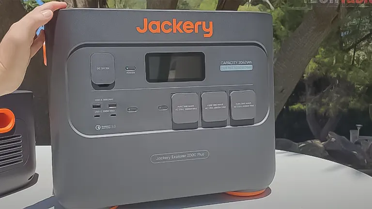 A Jackery Explorer 2000 Pro solar generator with a digital display and various power outlets, held by a hand