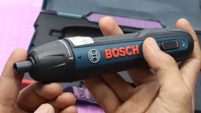 Hands holding Bosch Go Smart Screwdriver over pink grid