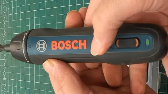 Hand holding Bosch Go Smart Screwdriver over gridded mat