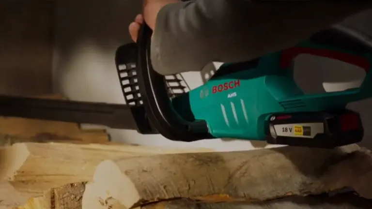 Person lifting the Bosch AHS 50-20 LI Cordless Hedge Trimmer in the top of the logs